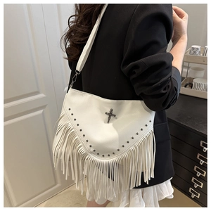 Détail d'un sac bandoulière blanc avec franges longues, breloque croix et rivets en métal