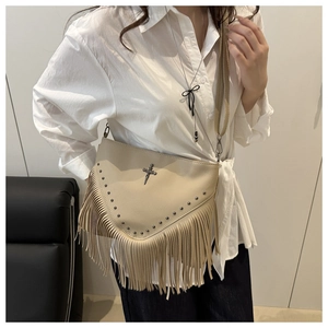 Gros plan d'un sac bandoulière beige à franges avec clous en V et logo en métal sur mannequin