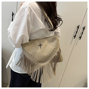 Détail d'un sac porté épaule beige à rivets avec franges et pendentif croix sur modèle