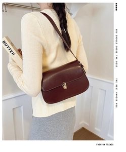 Detail of a burgundy patent leather crossbody bag with gold metal buckle and long strap