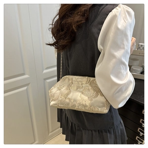 Close-up of elegant floral embroidery on a cream shoulder bag with gold chain strap