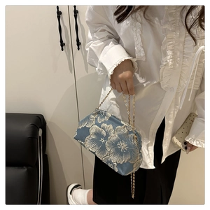 Détail de la pochette en satin bleu avec jacquard floral doré et fine chaîne en métal