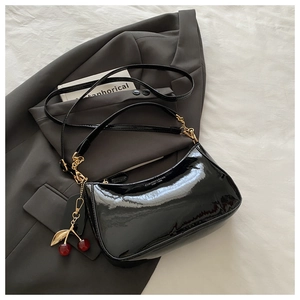 Détail du sac en cuir verni noir avec chaîne dorée et breloque cerise sur un costume