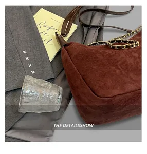 Detail of a brown suede shoulder bag with leather strap and golden chain on a grey blazer