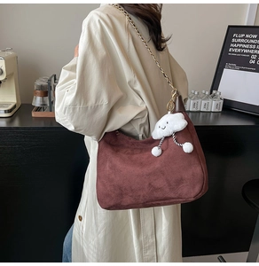 Detail of brown suede tote bag featuring a gold chain strap and fluffy white cloud pendant