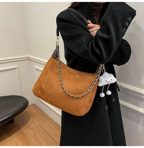 Detail of caramel suede tote bag with chain strap and soft white plush charm on black coat
