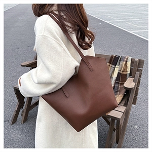 Outdoor shot of a large brown leather tote bag carried on a model's shoulder over a white coat