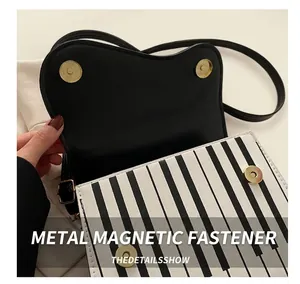 Close-up of golden magnetic buckle and piano key pattern on stylish crossbody bag