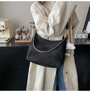 Detail of black suede tote bag with gold chain and white plush cloud charm on model