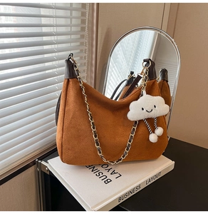 Detail of brown suede tote with gold chain strap and cute cloud charm on white books