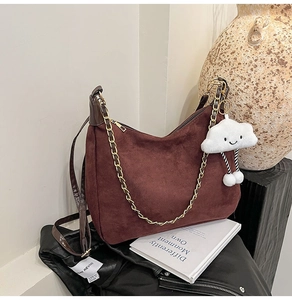 Detail view of brown suede tote bag featuring gold chain and white plush cloud charm
