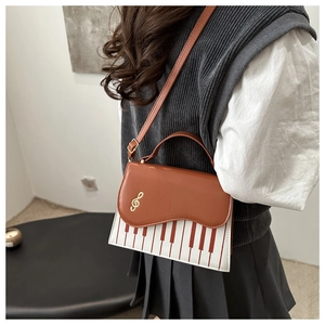 Detail of piano theme handbag featuring brown leather flap and golden treble clef metal logo