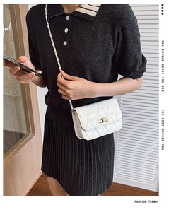 Close-up of white quilted mini bag with gold twist lock and woven metal chain strap