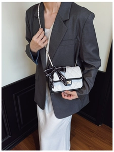 Detail of white quilted handbag featuring black trim, gold twist lock, and H-silk scarf bow
