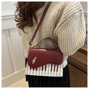 Detail view of burgundy piano keyboard handbag featuring gold treble clef metal decoration