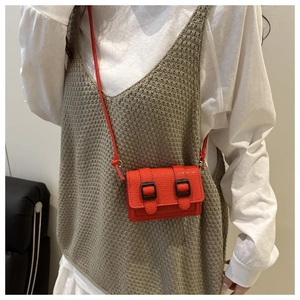 Dettaglio mini borsa a tracolla rossa con trama litchi e fibbie nere sulla modella