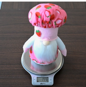 Detailed view of a plush strawberry chef gnome being weighed on a kitchen scale