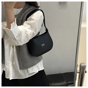 Detail showing a black leather shoulder bag with a silver bow decoration on a model
