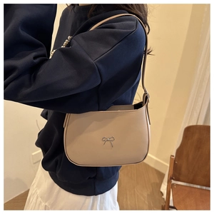 Side view of beige leather shoulder bag with delicate silver bow charm detail on model