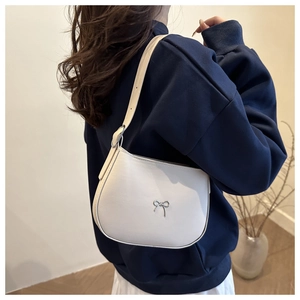Detailed side view of a white leather shoulder bag with silver bow detail worn by model