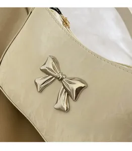 Detail of beige wrinkled leather bag featuring a 3D silver bow and sleek zipper closure