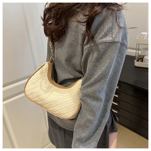 Detail of a crescent-shaped straw shoulder bag with brown leather trim and gold zipper