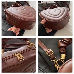 Detail view of heart-shaped handbag featuring pleated handle and gold zipper hardware