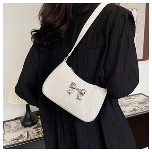 Detail of white textured leather underarm bag with silver metallic bow and chain strap
