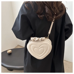 Detail of a cream heart-shaped crossbody bag with pleated ruffles and quilted texture