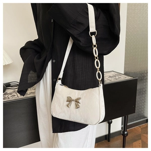Detail of white glossy pleated underarm bag with silver bow accent and chain strap