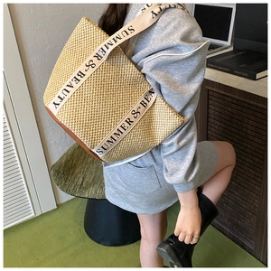 Detail view of woven straw tote bag with beige canvas straps and leather base