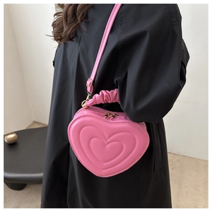 Pink heart-shaped crossbody bag featuring quilted faux leather and ruffled top handle detail