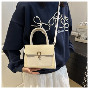 Detail of cream crossbody bag featuring woven texture flap and golden horseshoe lock