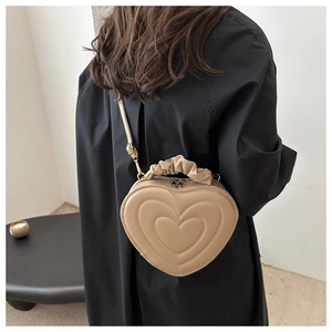 Model wearing a heart-shaped crossbody bag with pleated handle in beige faux leather