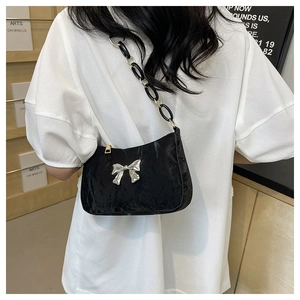 Detail of black pleated shoulder bag with silver bow buckle and gold chain strap