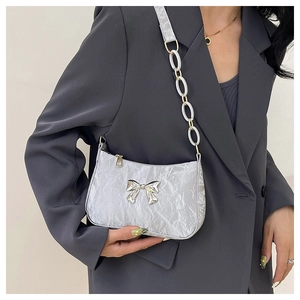 Detail of silver pleated underarm bag with metal bow and chunky chain strap on a blazer