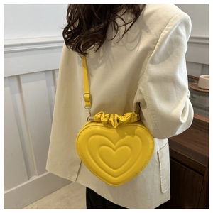 Detail of a bright yellow heart-shaped bag with pleated textures and metallic hardware