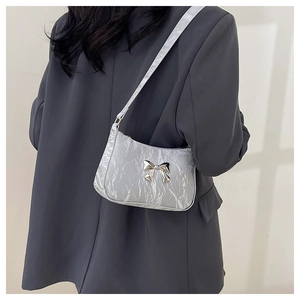 Silver shoulder bag with bow detail and crinkled texture shown on grey blazer