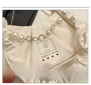 Détail du sac plissé blanc crème avec bandoulière en perles et fleurs métalliques