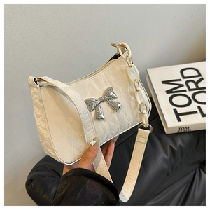 Detail of white wrinkled faux leather bag featuring a silver metal bow and acrylic chain