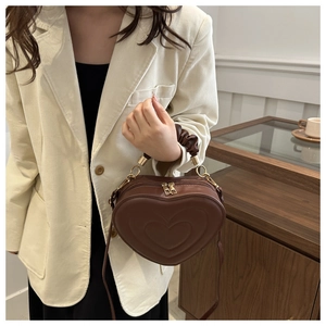 Detail of heart-shaped dark brown handbag with pleated handle and golden metallic zipper
