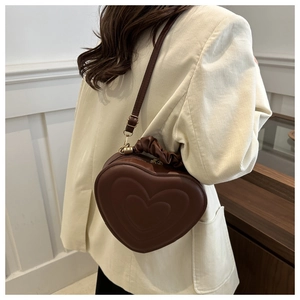 Brown heart-shaped crossbody bag with pleated handle and quilted design on model
