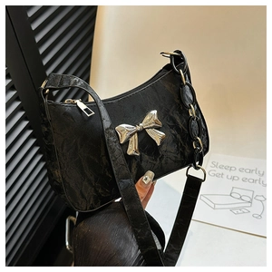 Close-up of black pleated hobo bag with silver metallic bow and chunky acrylic chain strap