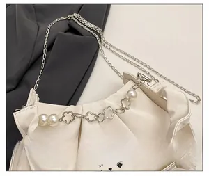 Détail d'un sac froncé blanc avec de grosses perles et des breloques fleurs argentées