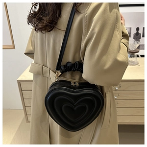Detail of heart-shaped quilted handbag with gathered handle and gold zippers on a model