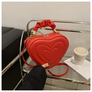 Close-up of a red heart-shaped leather bag with unique pleated handle and gold hardware