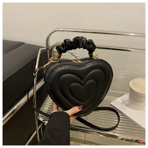Detail of heart-shaped black leather bag with pleated handle and gold hardware zipper