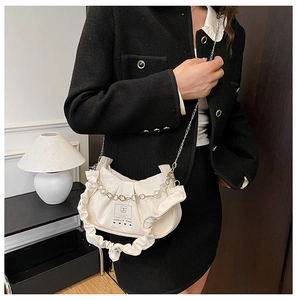 Détail du sac bandoulière plissé crème avec chaîne en perles et étiquette chic