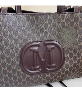 Close-up of brown letter M monogram print and embossed leather patch on large tote bag