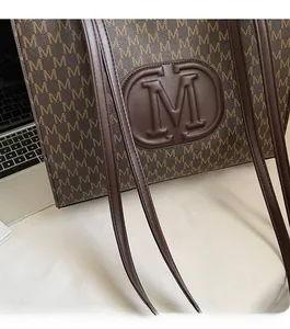 Detail of deep brown tote bag featuring M-monogram print and embossed leather patch
